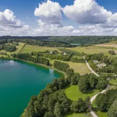 Widok z lotu ptaka na turkusowe jezioro, zielone wzgórza i lasy, z kilkoma domami.