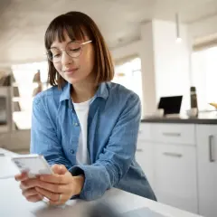 Kobieta w okularach przegląda telefon w nowoczesnej kuchni.