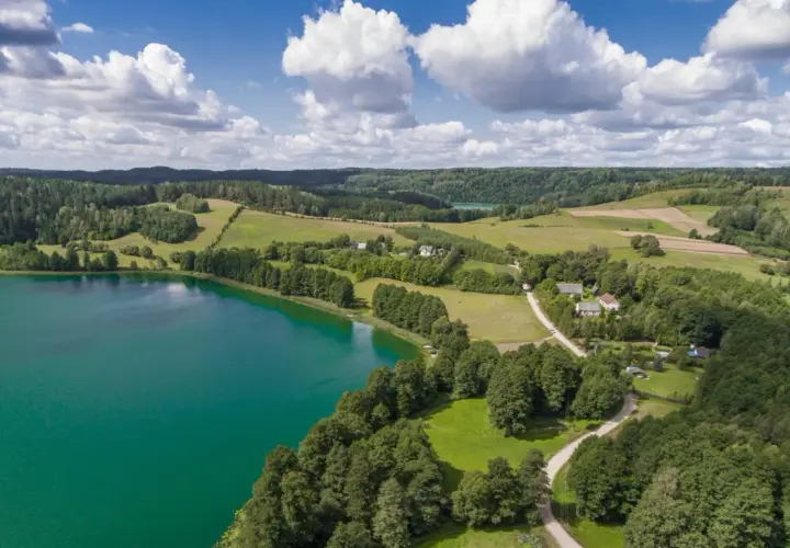 Widok z lotu ptaka na turkusowe jezioro, zielone wzgórza i lasy, z kilkoma domami.